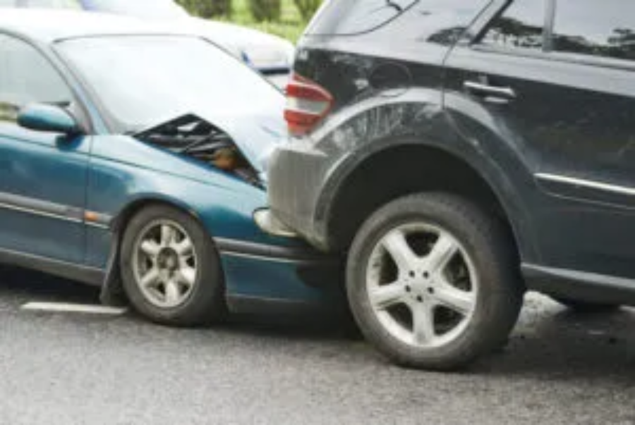 A close-up shot of a two-car collision where a teal sedan has rear-ended a dark SUV. The hood of the sedan is crumpled upward from the impact against the SUV's rear bumper.