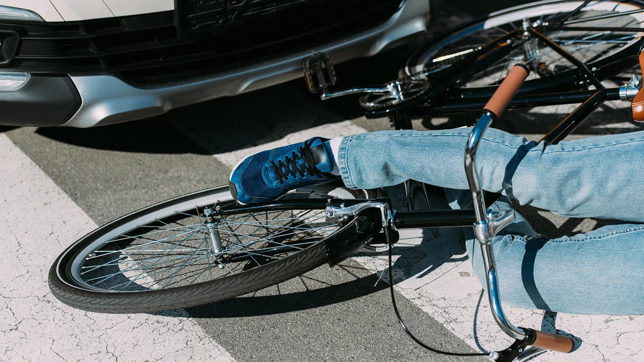 Cyclist lying on the road next to a bicycle after a collision with a car at a crosswalk.