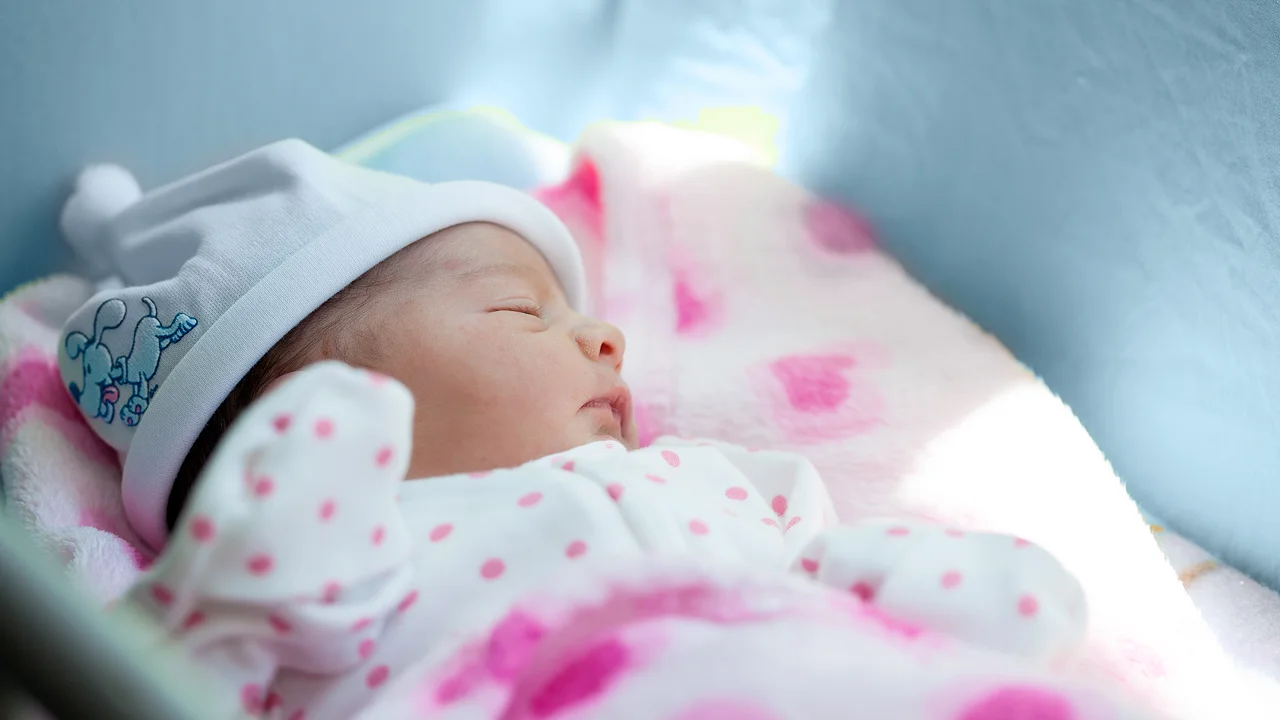 Newborn baby in a beanie sleeping in a pink blanket.