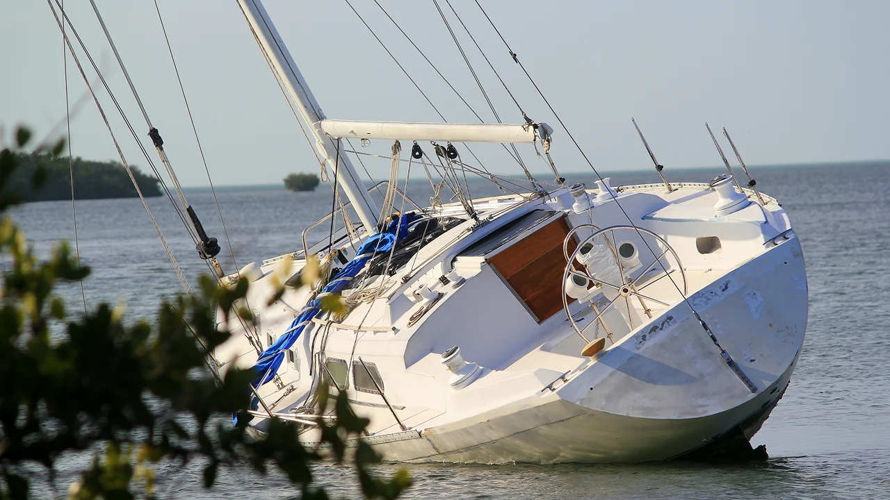 A white sailboat grounded on its side in shallow water near shore.