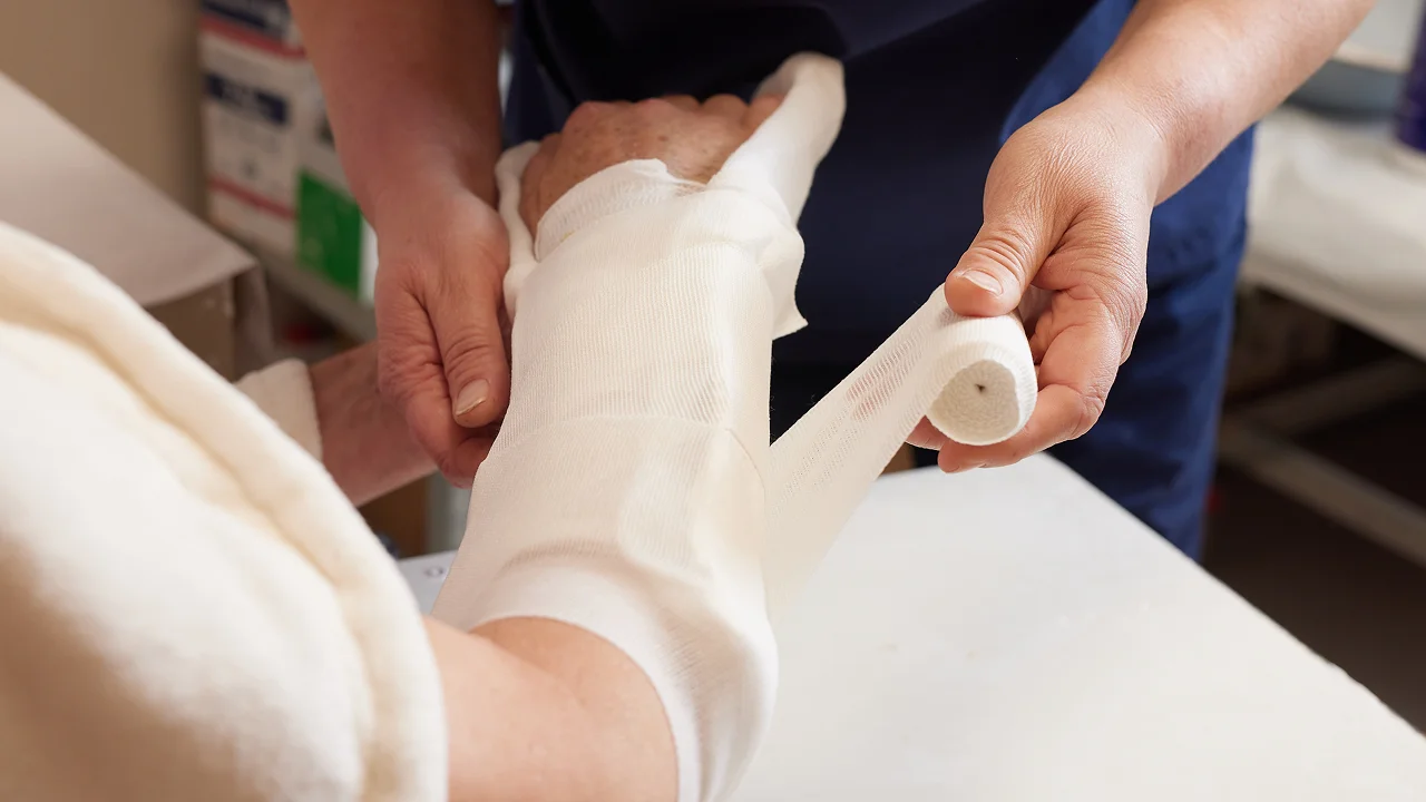 Medical worker bandaging a patient's hand and wrist.