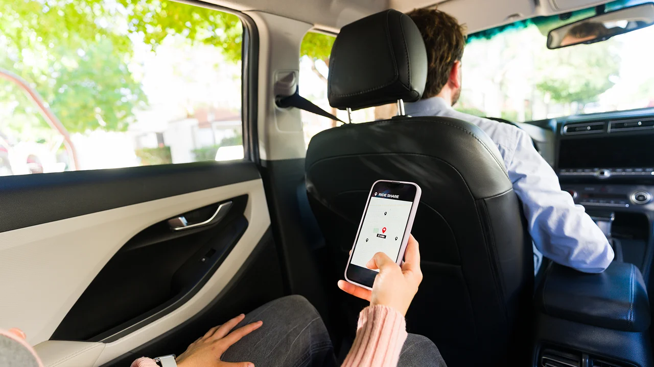 Passenger in the back seat of a rideshare car using a mobile app on their phone.