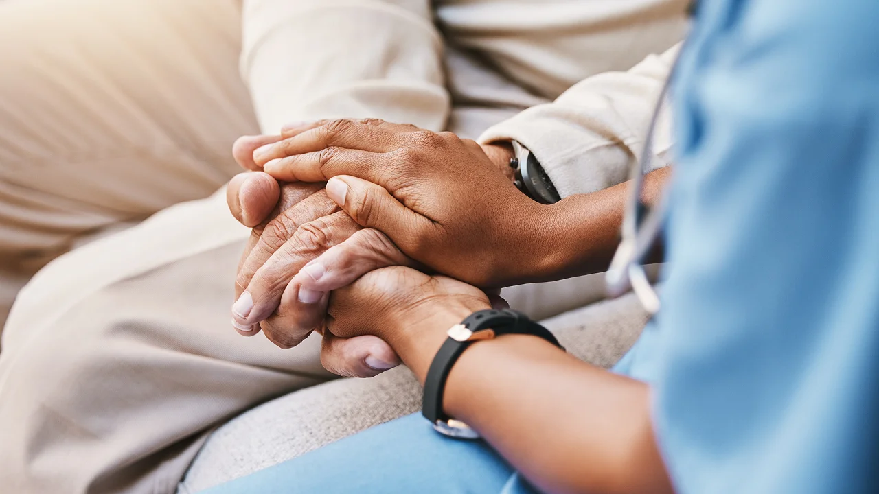 Healthcare worker holding hands with an elderly patient in support.