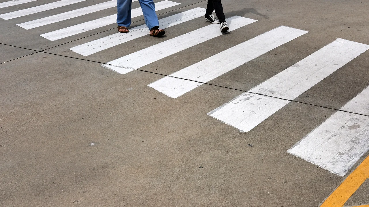 Pedestrians walking across a white striped crosswalk.
