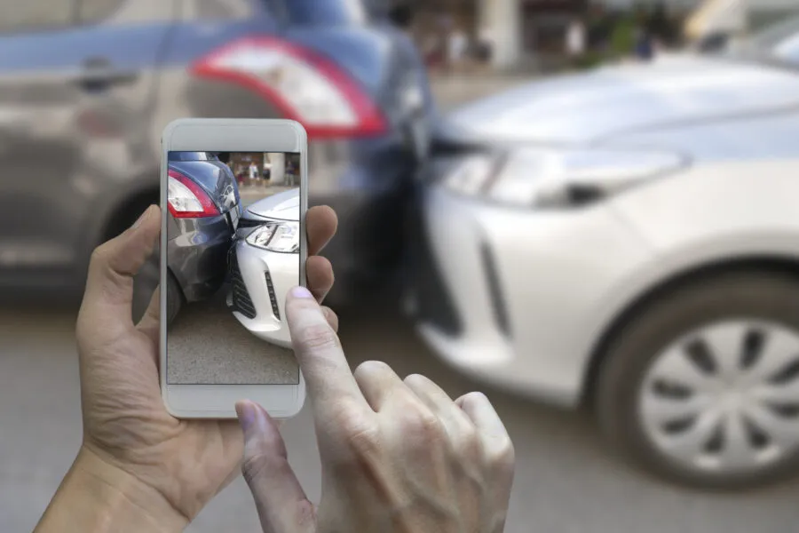 The image shows a person using a smartphone to take a photo of a minor car accident involving two vehicles.