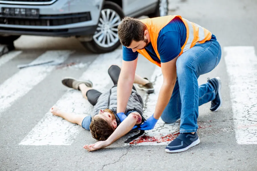 Man applying first aid to the injured bleeding person, wearing tourniquet on the arm after the road accident on the pedestrian crossing