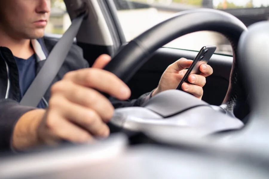 A driver holding a smartphone and texting while behind the steering wheel of a car.
