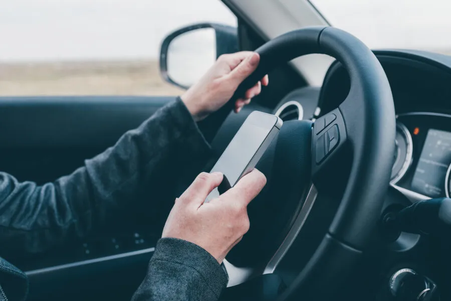 Texting and driving is dangerous behavior in traffic, close up of female hand typing text message on mobile phone while traveling through countryside with her car