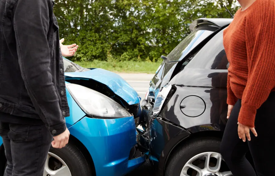 Two drivers standing next to their vehicles after a rear-end collision between a blue car and a black hatchback.