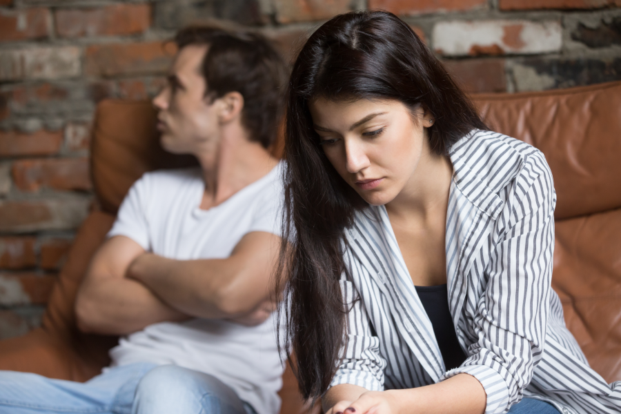 Sad pensive young girl thinking of relationships problems sitting on sofa with offended boyfriend, conflicts in marriage, upset couple after fight dispute, making decision of breaking up get divorced