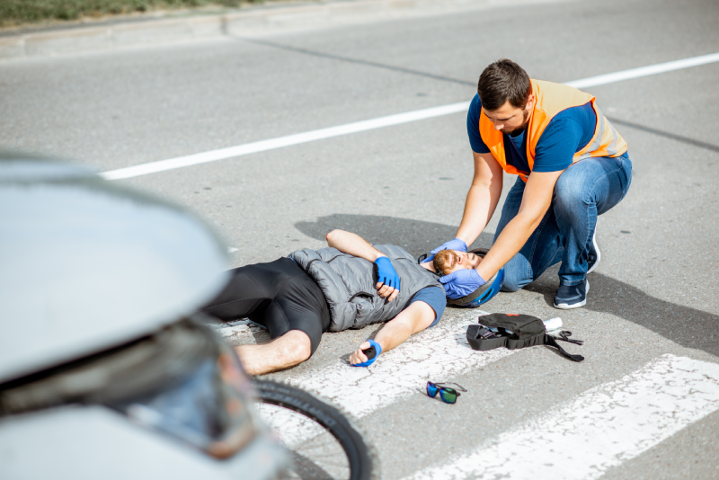 Road accident with injured cyclist on the pedestrian crossing with passerby pedestrian providing first aid fixing men's head