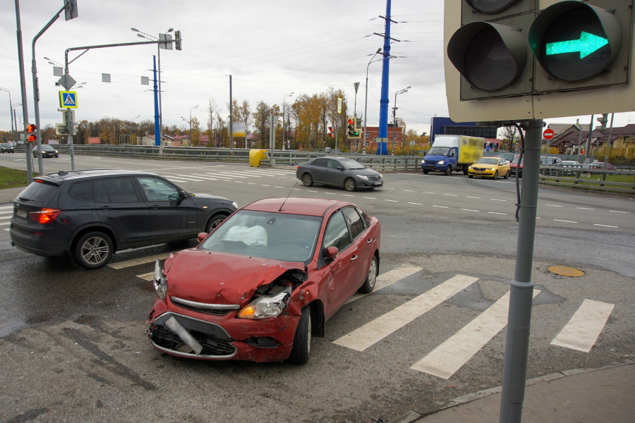 A red wrecked car stands at a crossroads against the backdrop of cars passing by. The concept of reckless and careless driving.