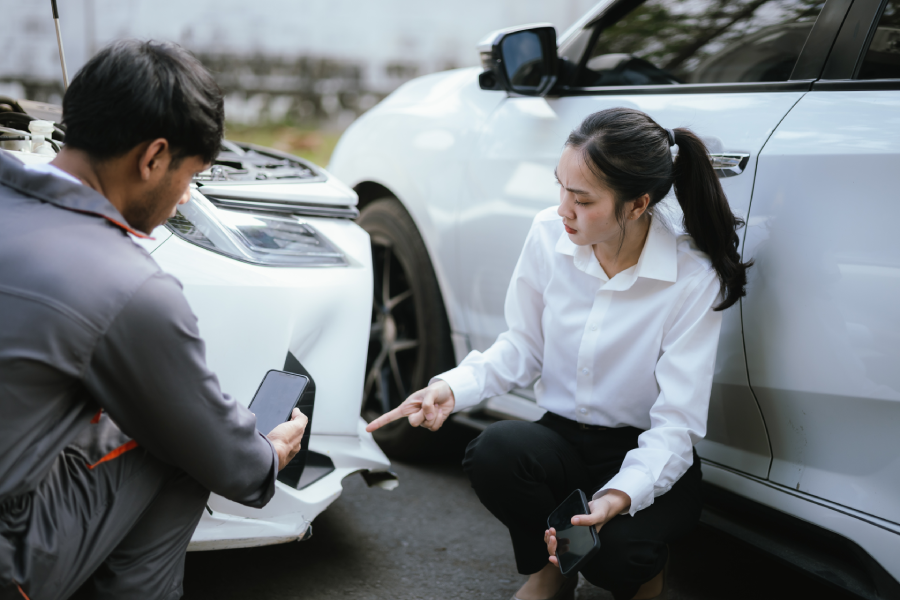 Insurance agent holding clipboard talking to car accident victim, inspecting damaged car parked on road after crash to analyze claim
