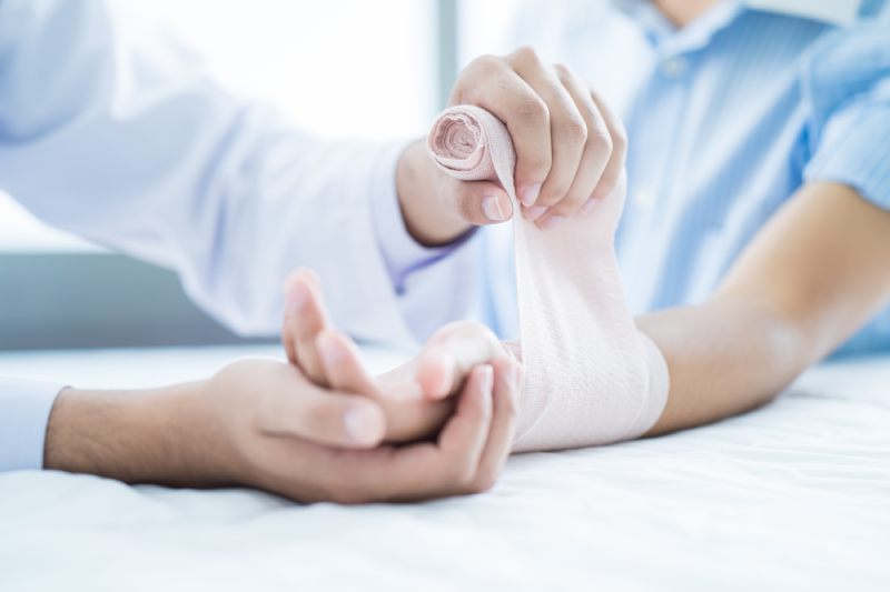 Close-up doctor is bandaging upper limb of patient.