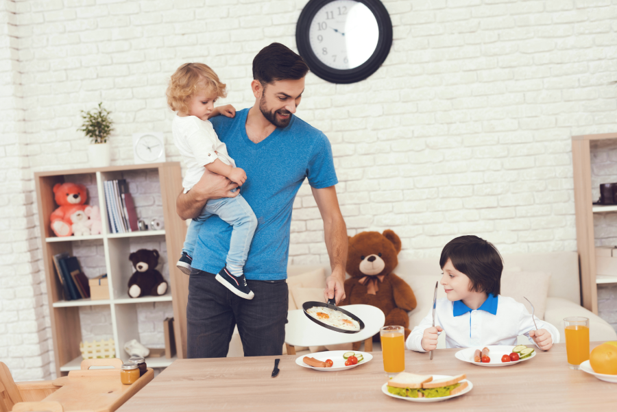 A man spends time with his sons. The father of two boys is engaged in raising children. Father feeds his son. Children have breakfast with their father.