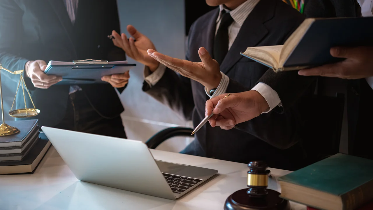 Lawyers or legal professionals discussing documents around a laptop and law books.